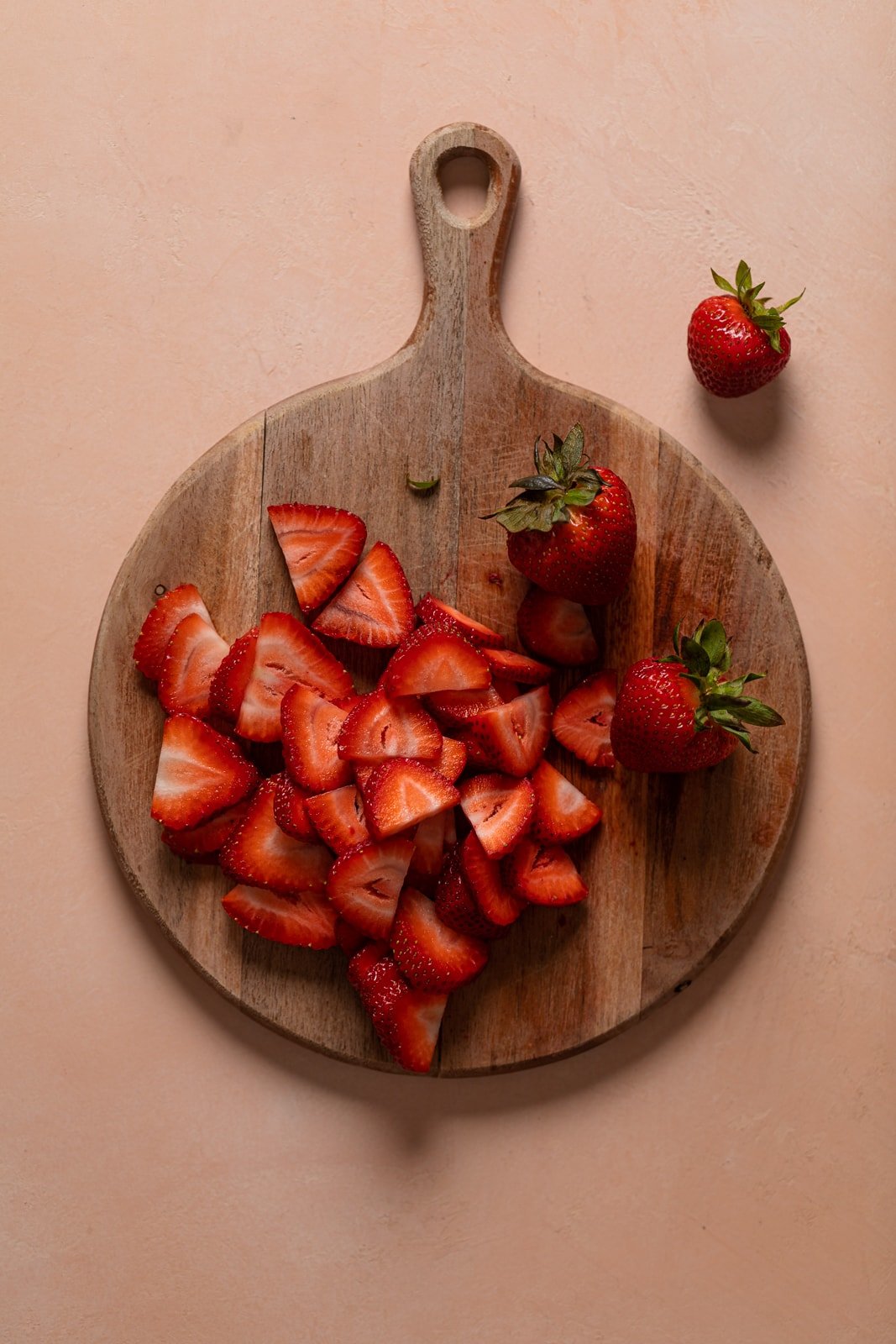 Strawberries and strawberry pieces on a wooden cutting board