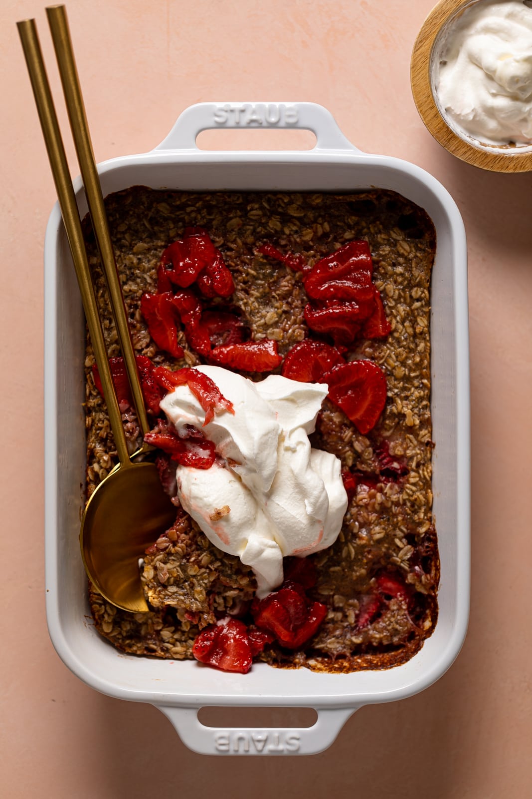 Pan of Strawberry Shortcake Baked Oats topped with strawberry sauce and coconut whipped cream