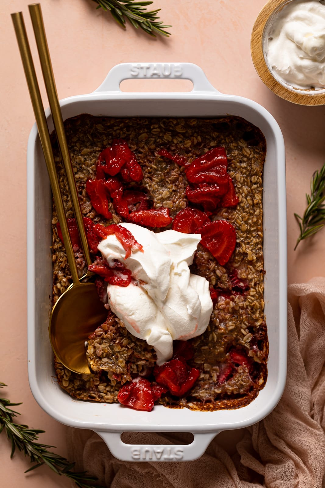 Pan of Strawberry Shortcake Baked Oats topped with strawberry sauce and coconut whipped cream