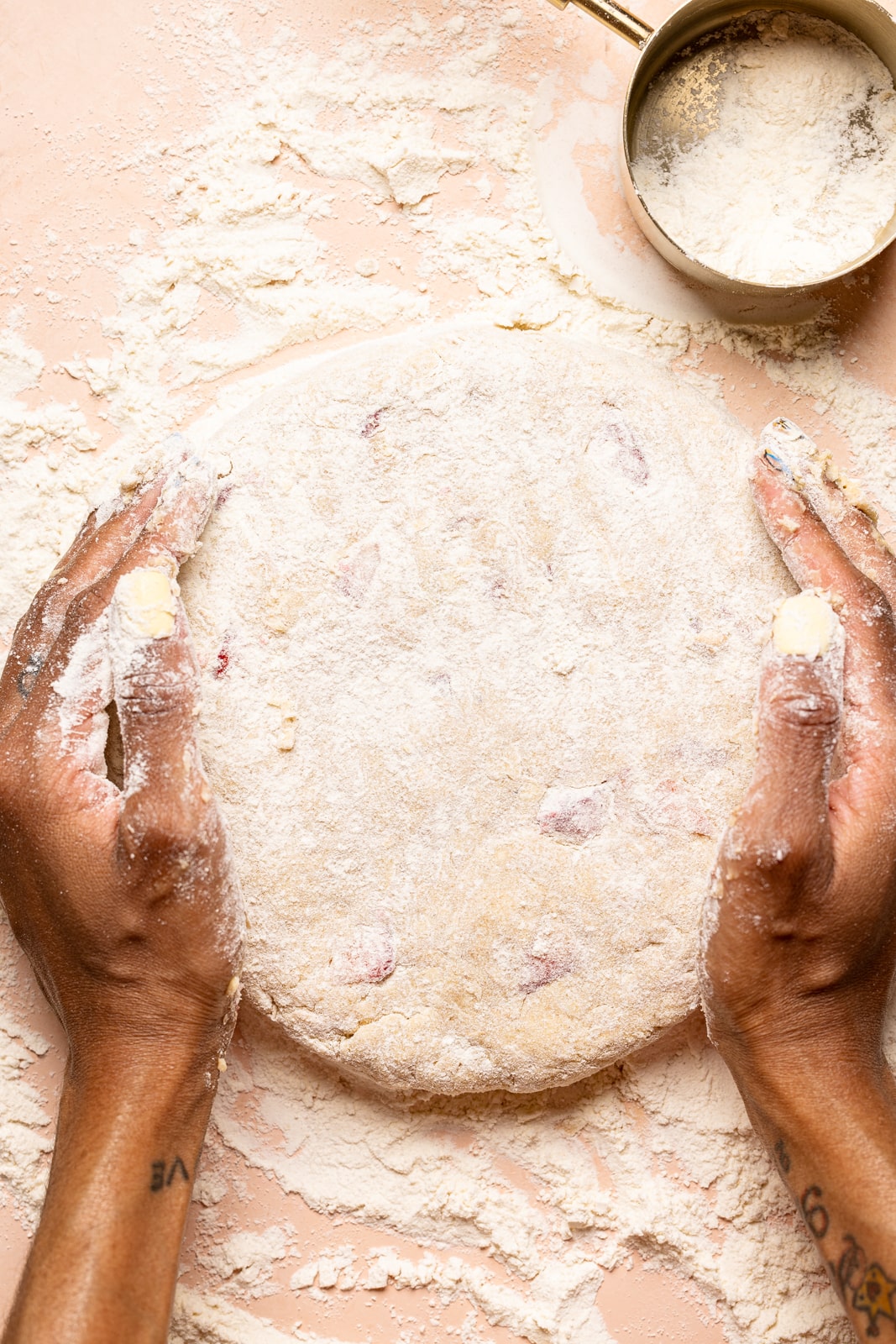 Scone dough on a floured surface with a measuring cup with flour being shaped into a circle.