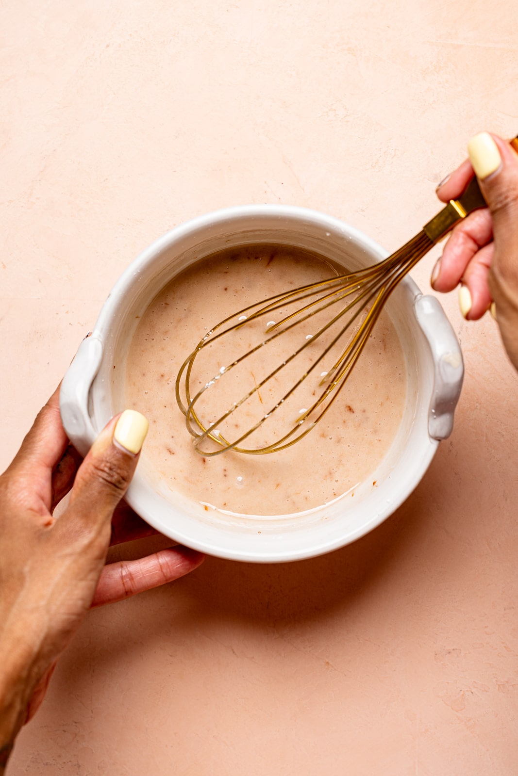 Strawberry glaze being whisked in a white bowl on a peach table.