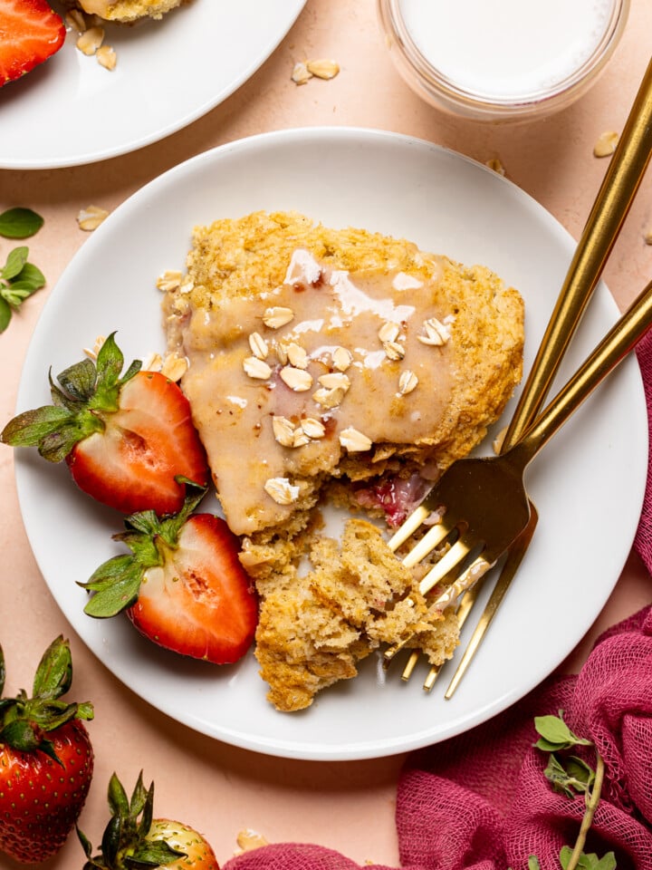 Baked scones on a white plate with two forks and sliced strawberries.