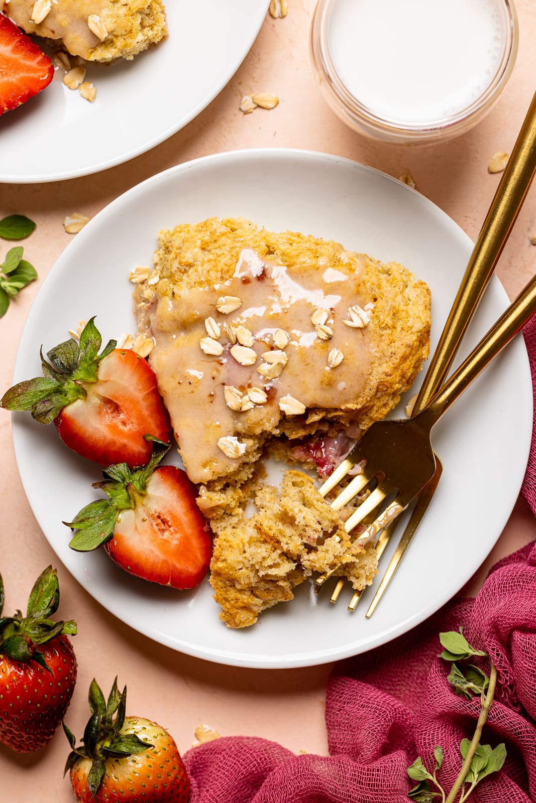 Baked scones on a white plate with two forks and sliced strawberries.