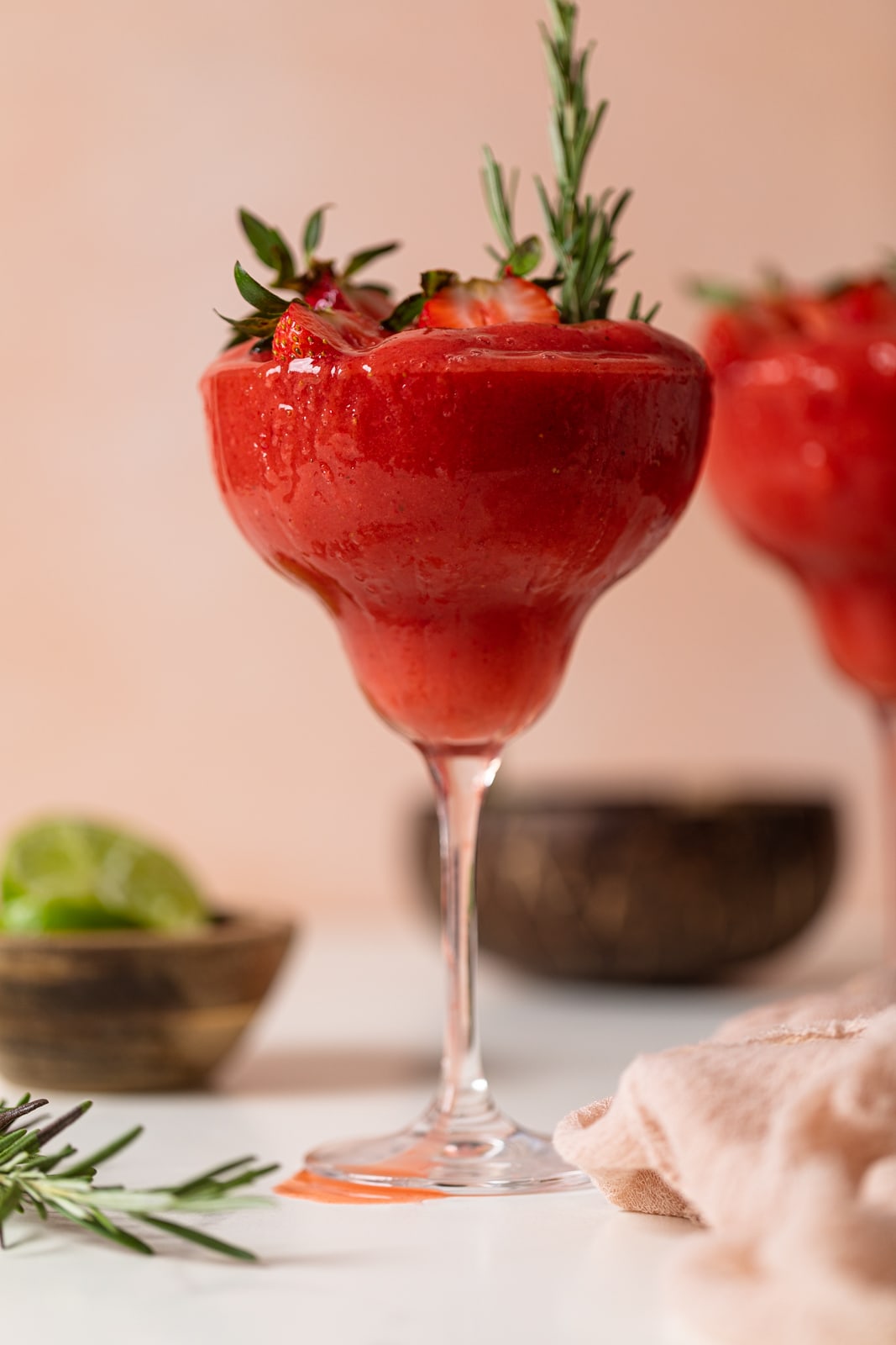 Frozen Cucumber Watermelon Strawberry Mocktail in a long-stemmed glass topped with halved strawberries and a sprig of rosemary