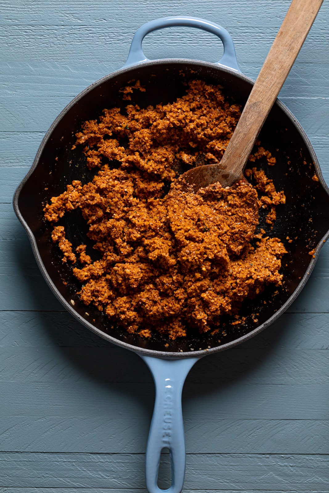 Wooden spoon stirring a skillet of seasoned walnut taco \"meat\"