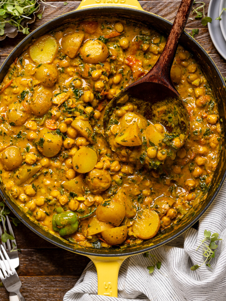 Image of Vegan Potato and Chickpea Curry in a skillet with a wooden spoon.