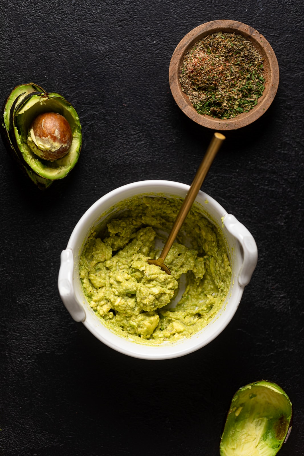 Bowl of mashed avocado with a spoon near a bowl of spices