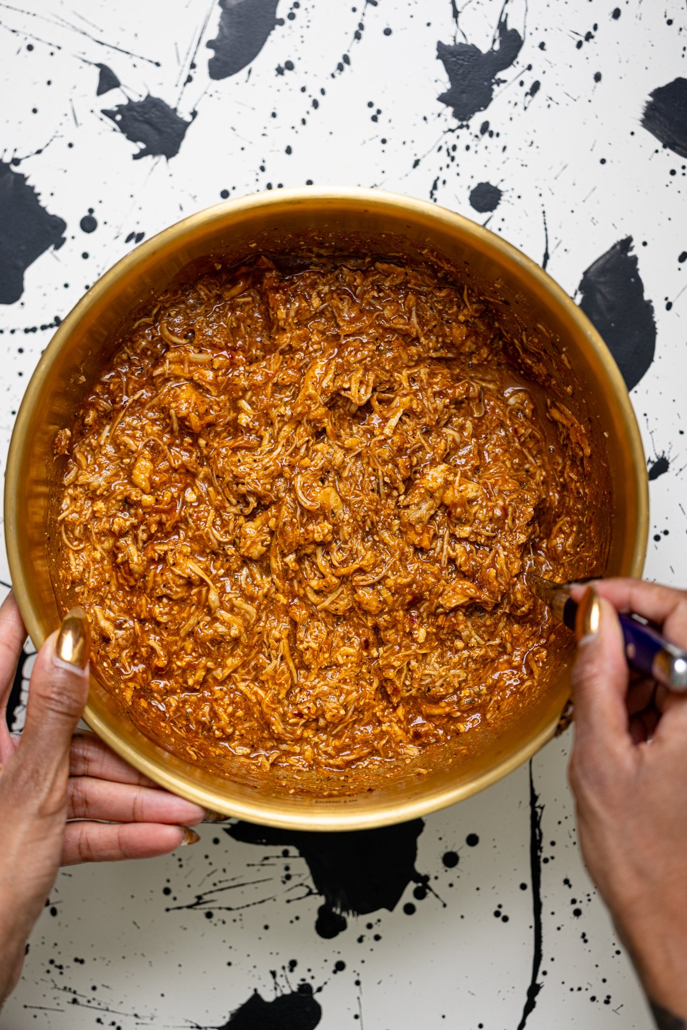 Shredded chicken with BBQ sauce in a bowl being stirred with woman hands.