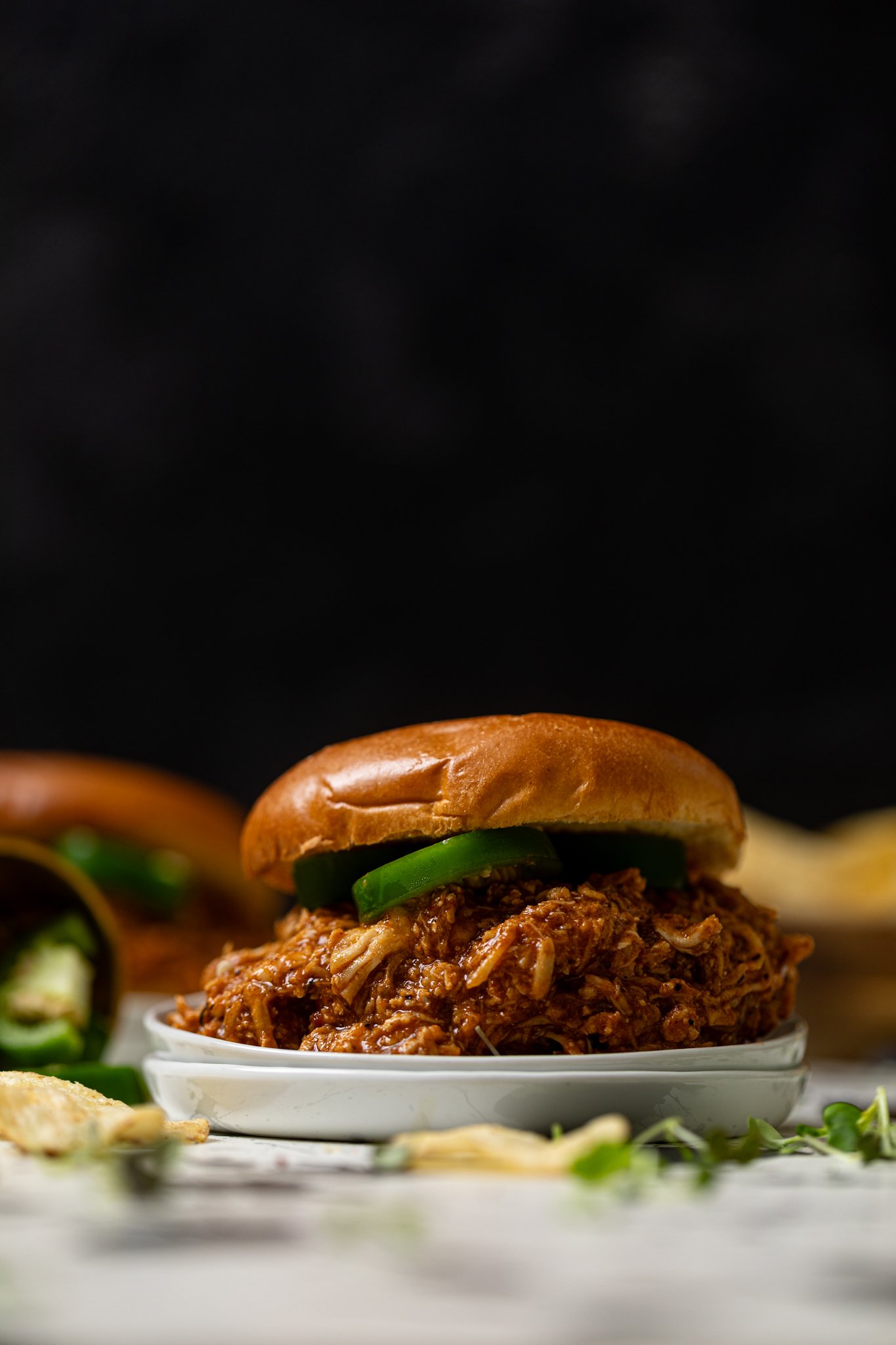 Best BBQ Pulled Chicken Sandwich on a white plate with chips and jalapenos.