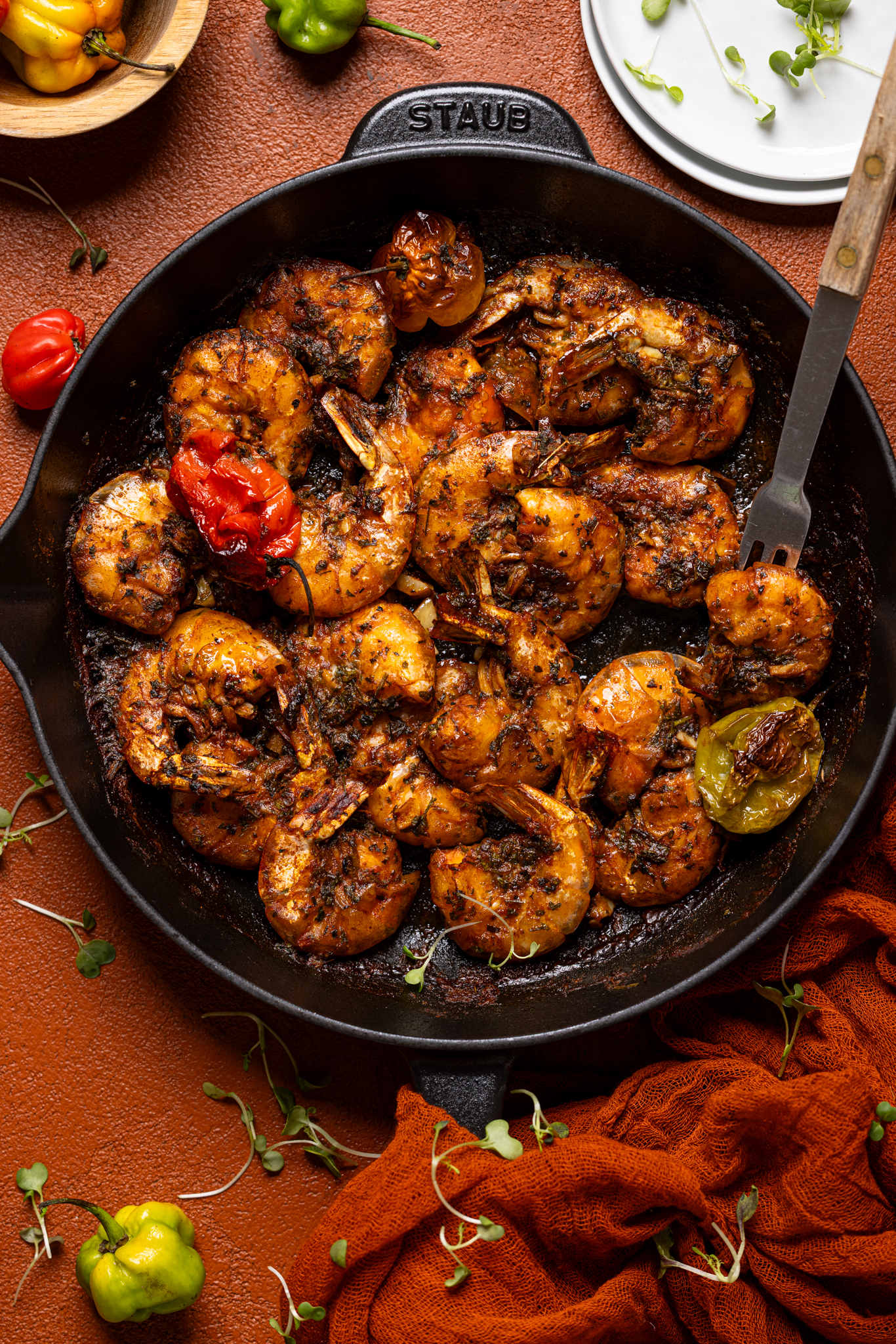 Jamaican Pepper Shrimp in a skillet with a fork, peppers, and white plates.