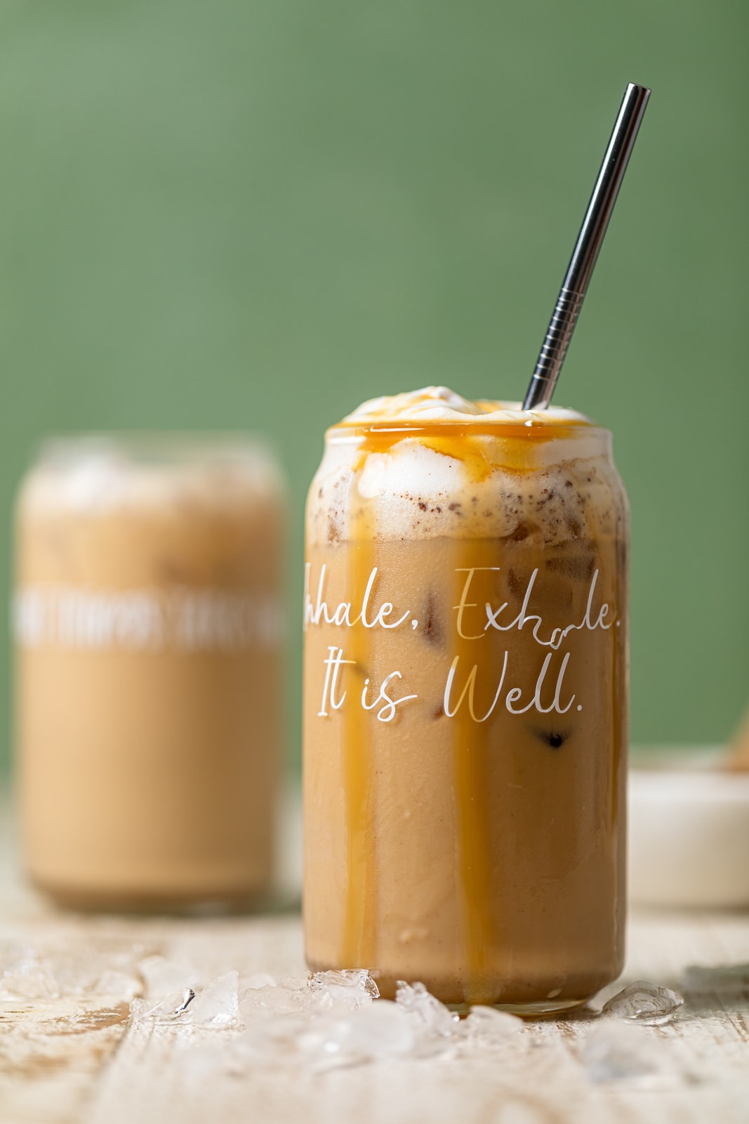 Peanut Butter Caramel Iced Latte with a straw in a glass with script that reads \"Inhale. Exhale. It is Well.\"