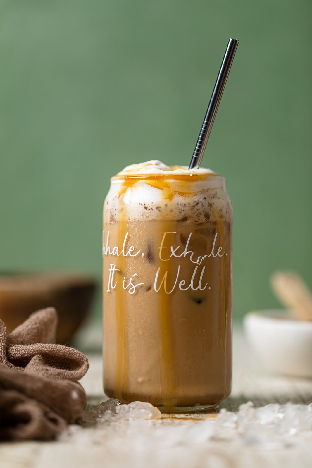 Peanut Butter Caramel Iced Latte in a glass overflowing with caramel and with script that reads \"Inhale. Exhale. It is Well.\"