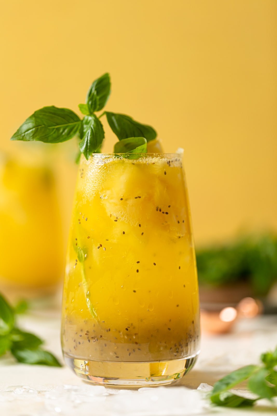 Glass of bright yellow Pineapple Chia Seed Tropical Mocktail topped with basil leaves