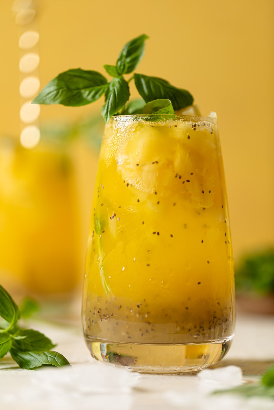 Glass of bright yellow Pineapple Chia Seed Tropical Mocktail topped with basil leaves