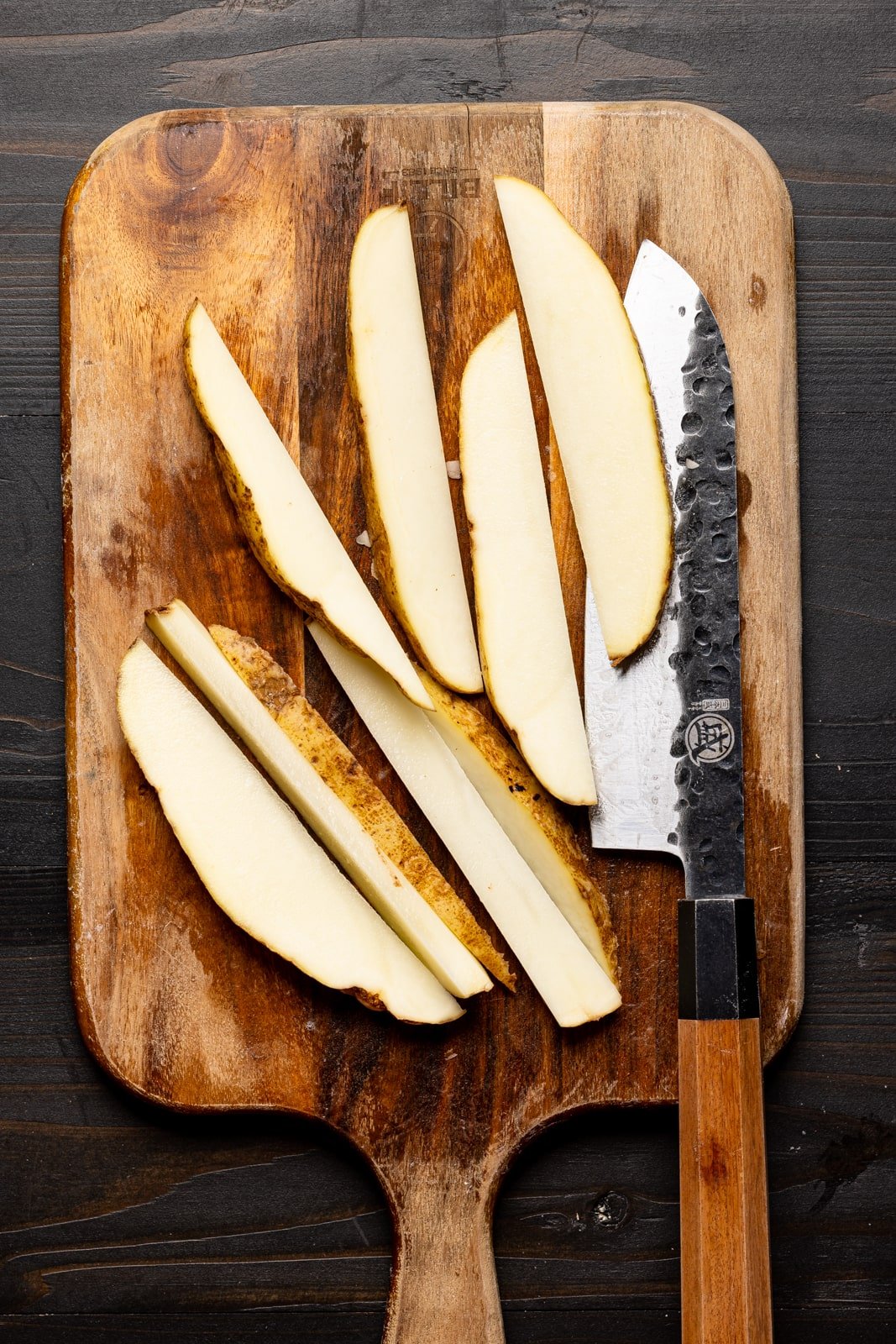 Russet potatoes cut lengthways on a cutting board with knife.