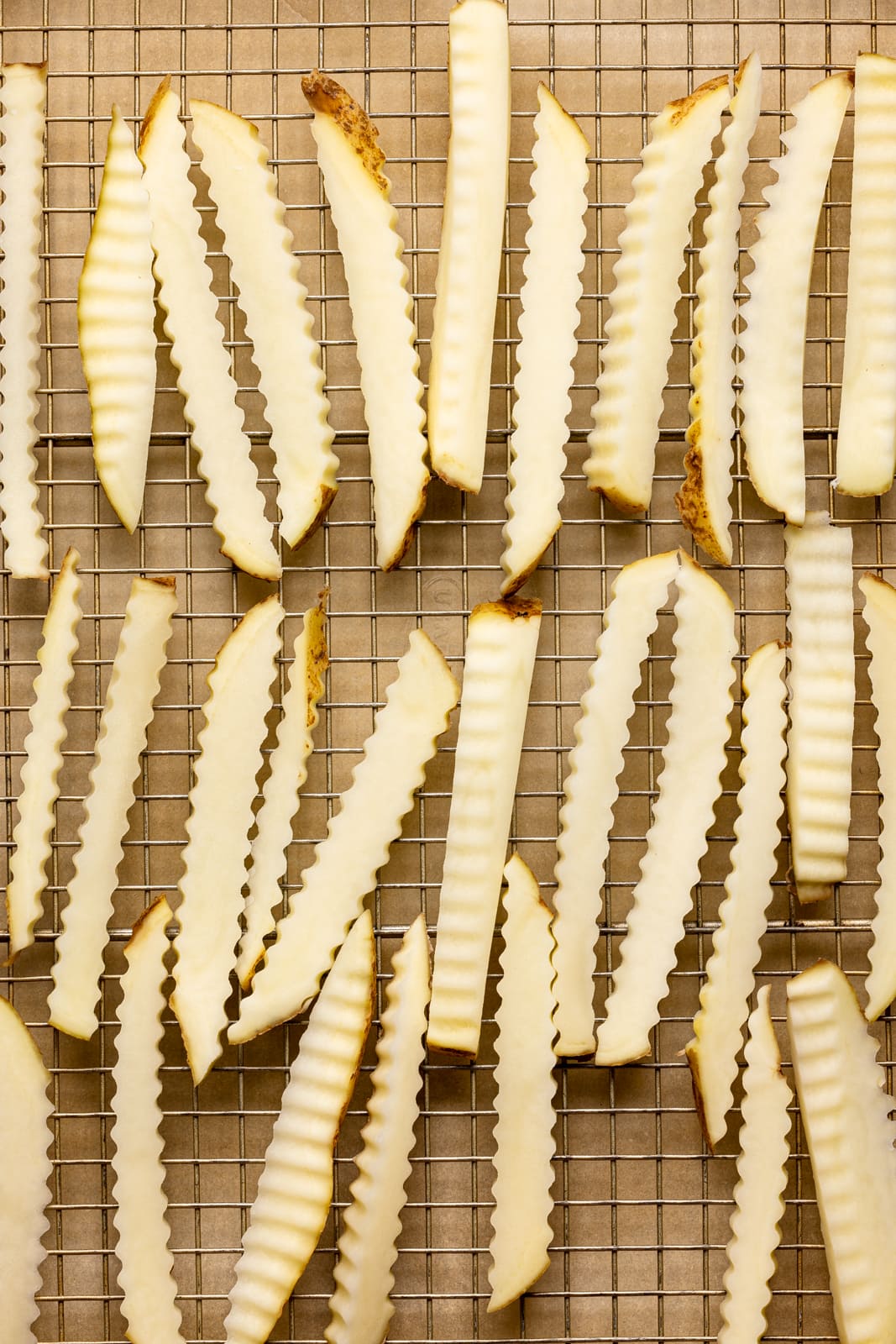 Fries cut in a crinkled shape lined side by side on a large baking sheet with parchment paper.