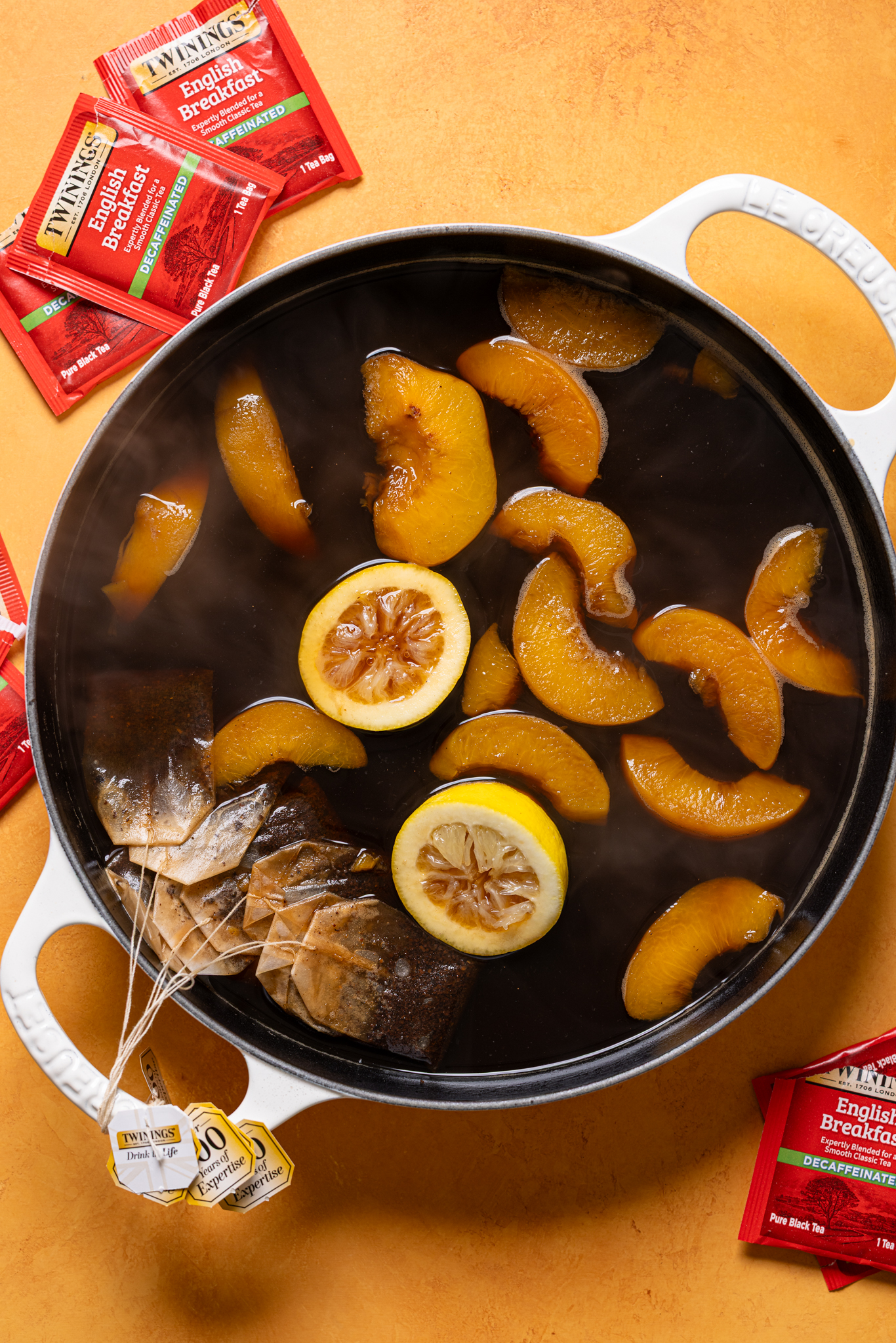 Peach sweet tea mixture in a white pot with teabags and lemons.
