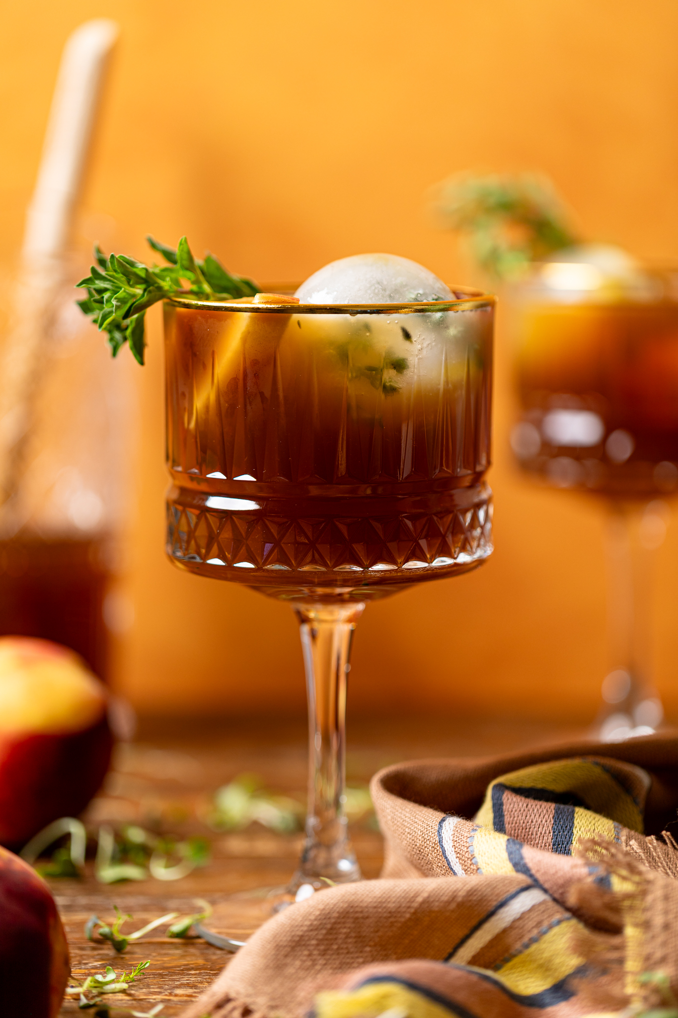 Image of peach sweet tea in two tall glasses on a brown wood table with peaches.
