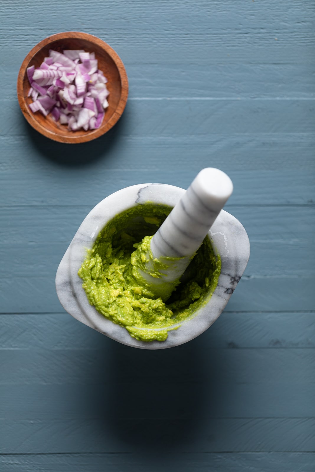 Mortal and pestle with mashed avocado near a small bowl of chopped red onion