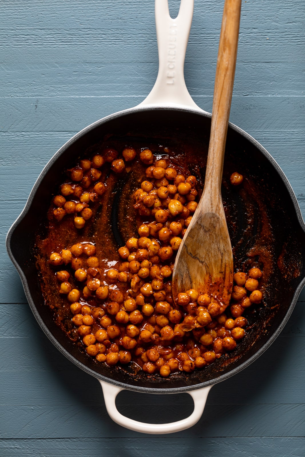 Wooden spoon stirring seasoned chickpeas in a skillet