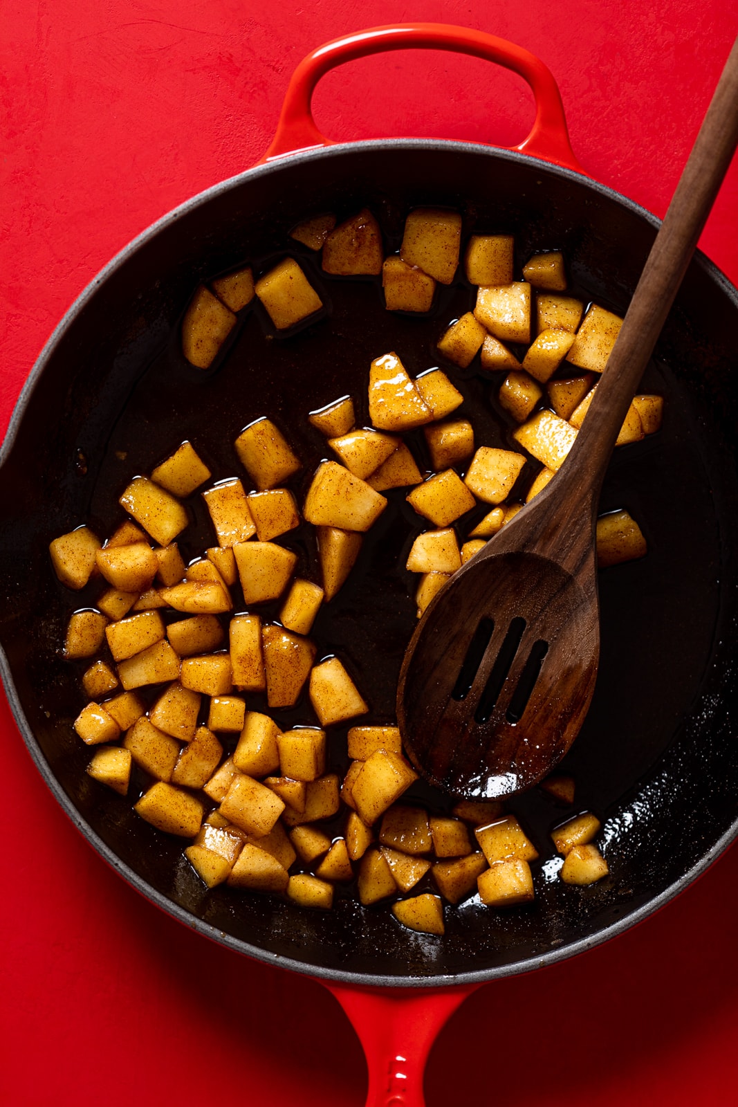 Wooden spoon stirring seasoned apple pieces in a skillet