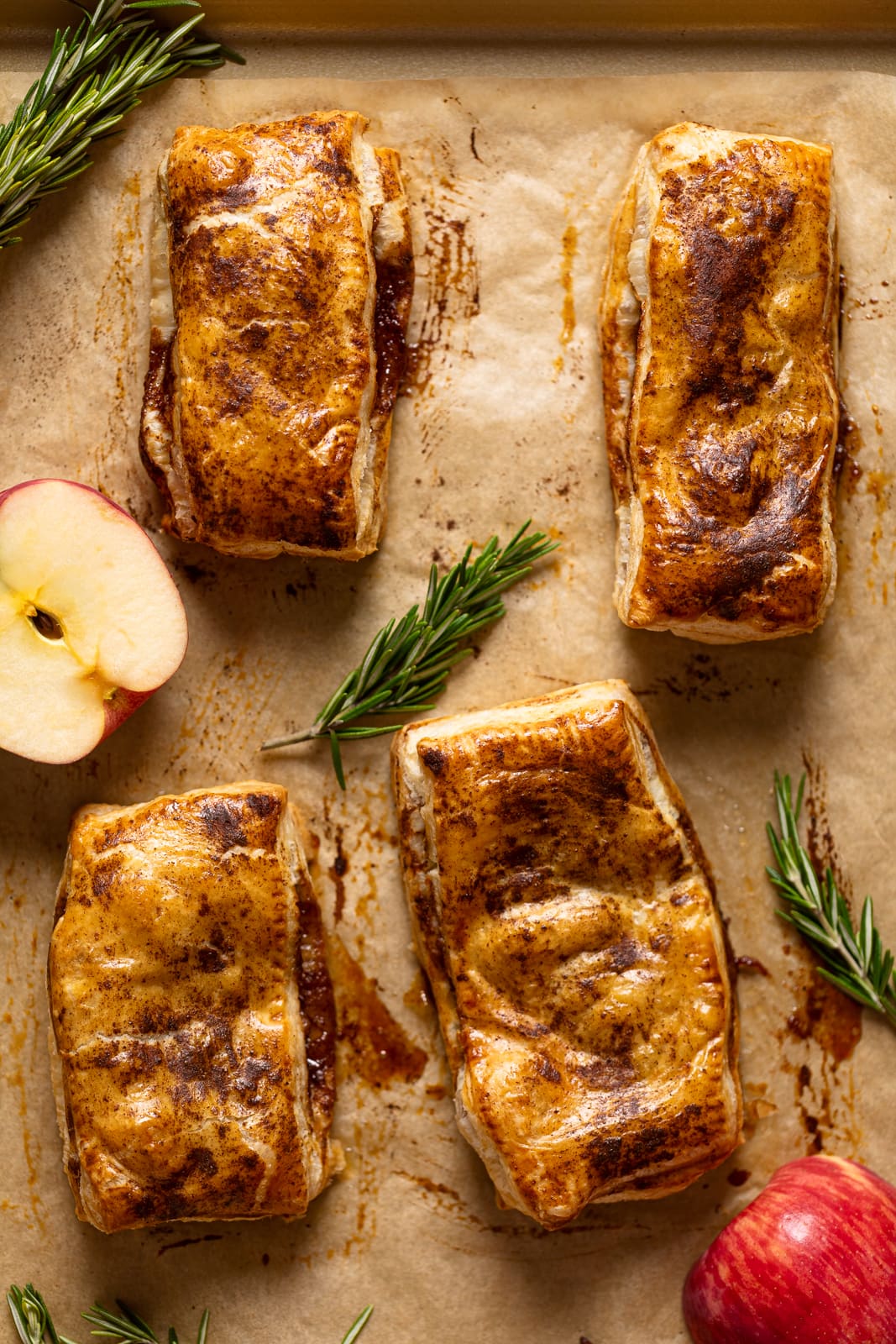 Apple Hand Pies on parchment paper with sprigs of rosemary and half an apple