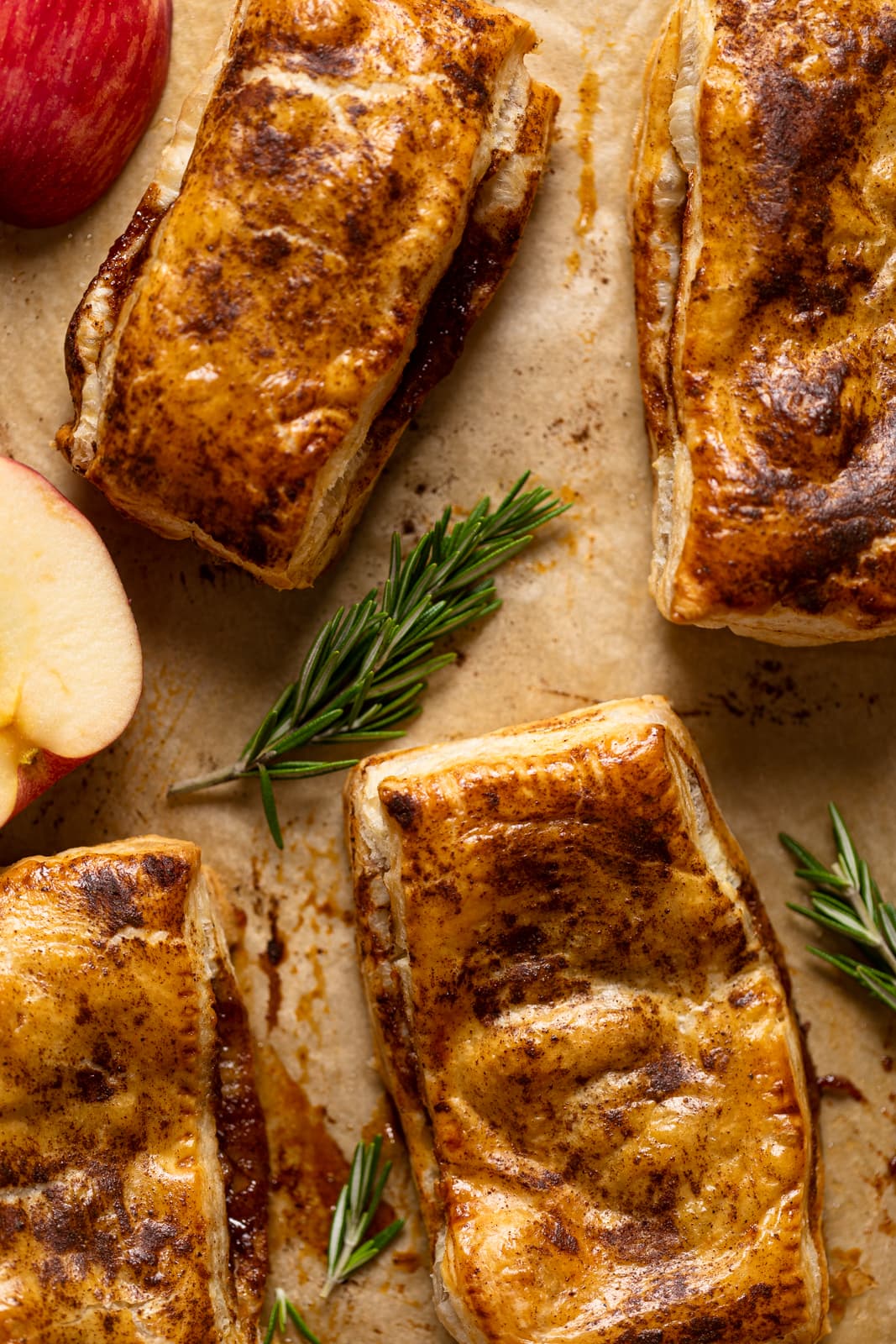 Apple Hand Pies on parchment paper with sprigs of rosemary and apple pieces