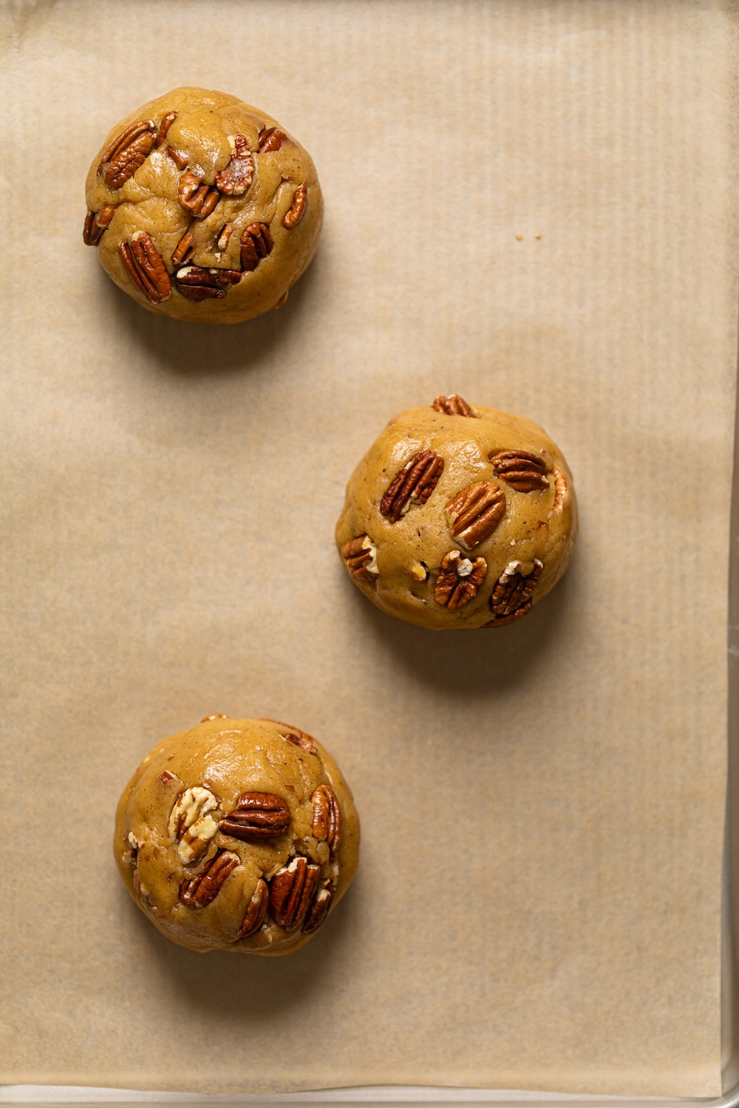 Balls of Chocolate Stuffed Butter Pecan Cookie dough on parchment paper