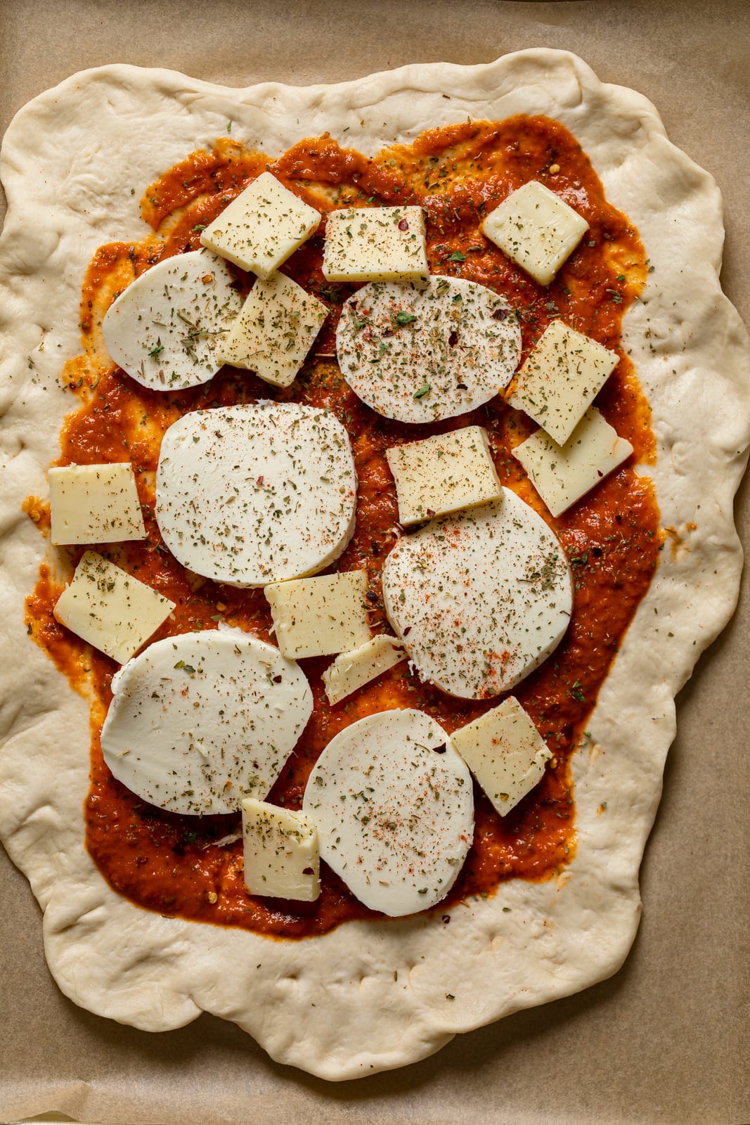 Uncooked pizza dough topped with sauce, cheese, and seasonings