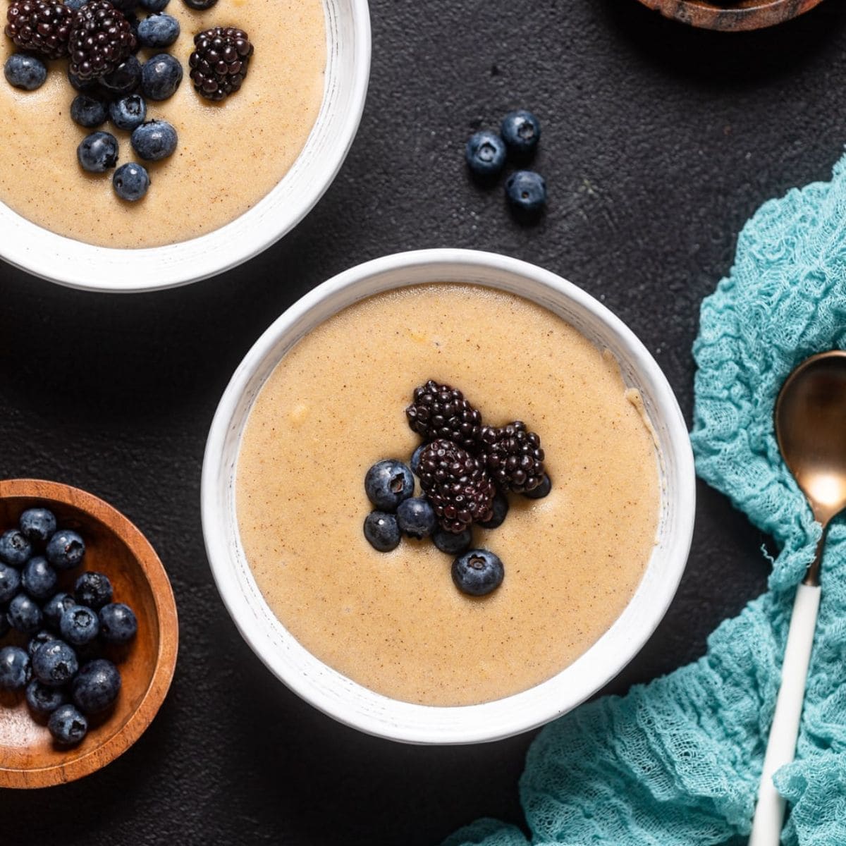 Porridge in two white bowls with a spoon and garnish of berries.