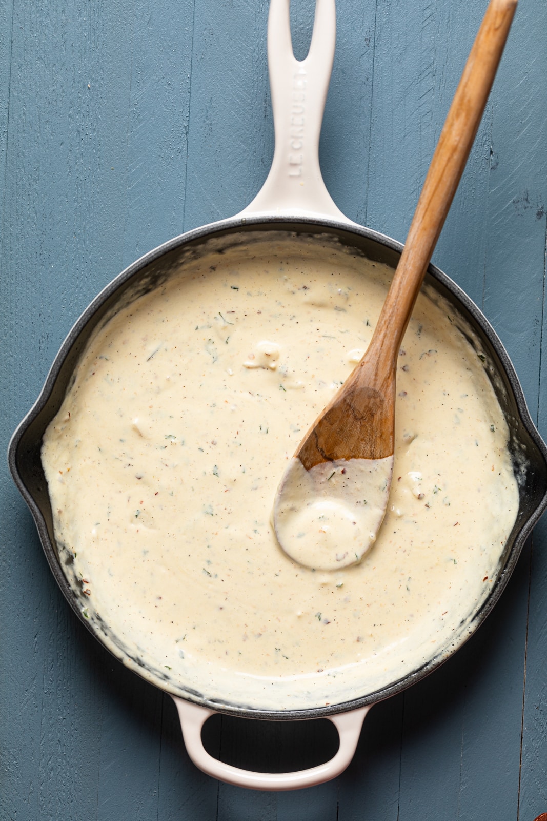 Wooden spoon in a skillet of white garlic sauce