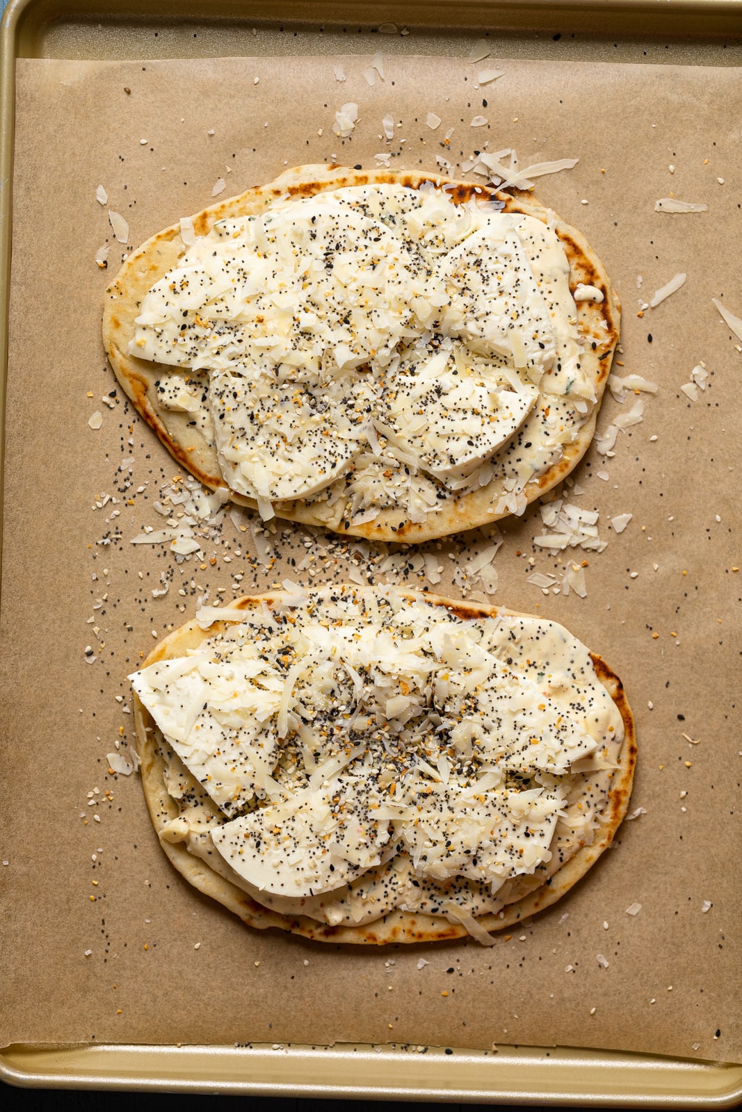 Two Everything Bagel Cheese Naan Pizzas on parchment paper