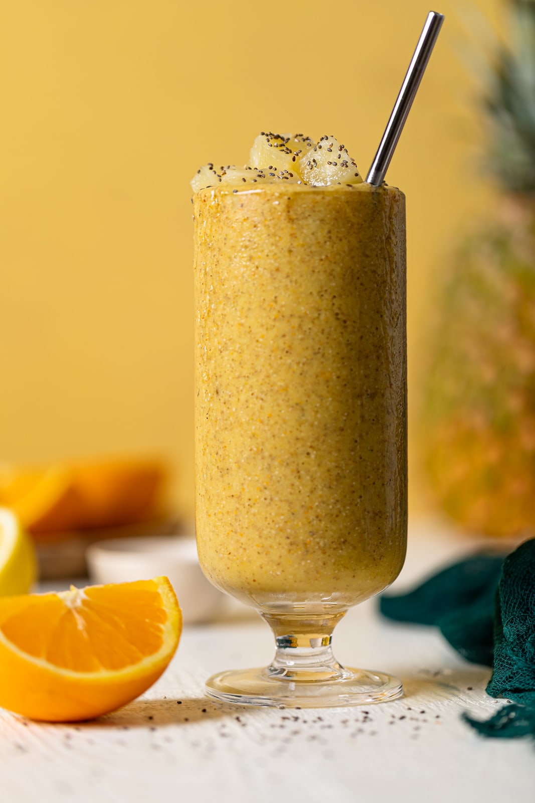 Glass of Pineapple Citrus Smoothie with a straw next to an orange wedge