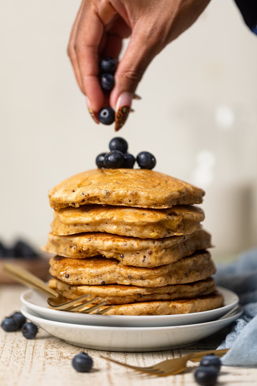 Hand adding blueberries on top of a stack of Fluffy Protein Pancakes