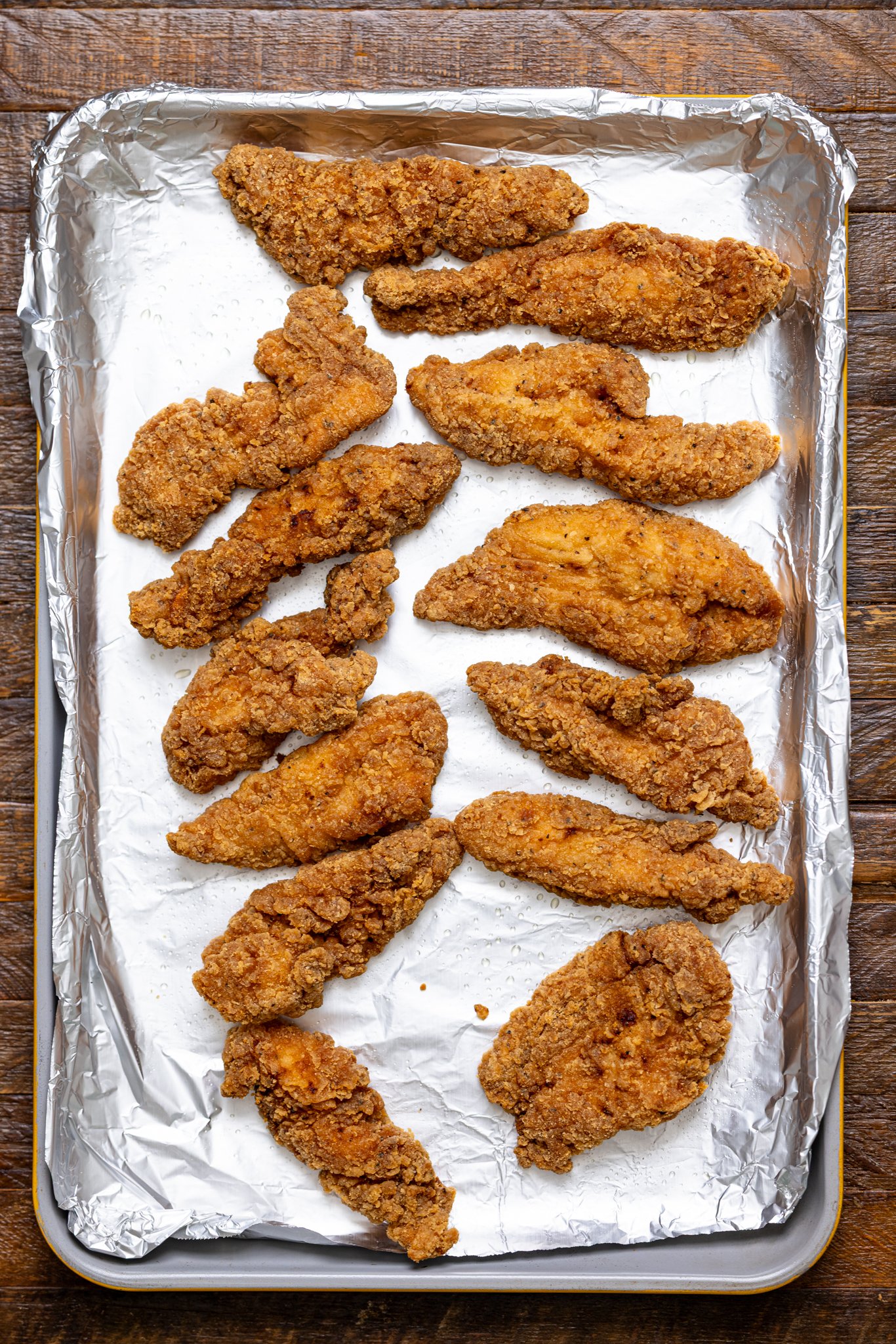 Baked crispy chicken tenders on a baking sheet with foil paper.