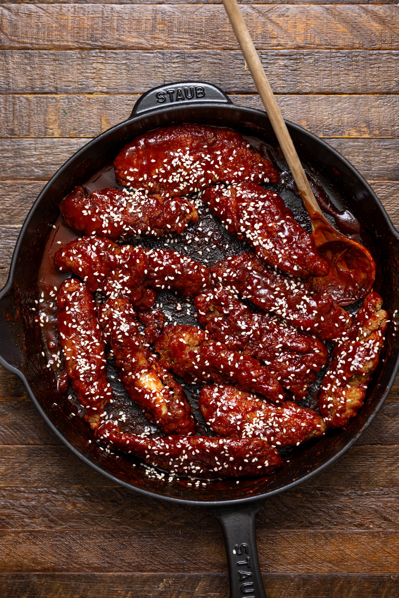 Delicious Gochujang Chicken Tenders in a black skillet with a wooden spoon.