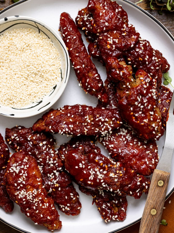 Delicious Gochujang Chicken Tenders on a white platter with a side of sesame seeds and a fork.