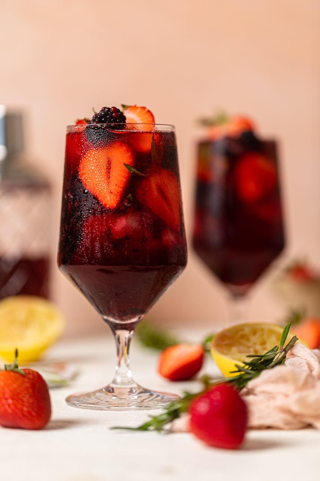 Glass full of fruit and dark red Loaded Hibiscus Mocktail near halved strawberries