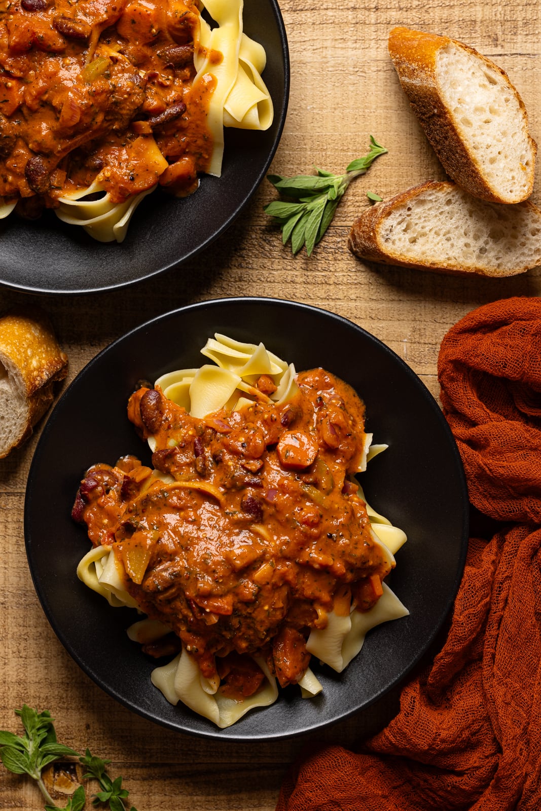 Vegan bolognese on two black plates with side of bread. 