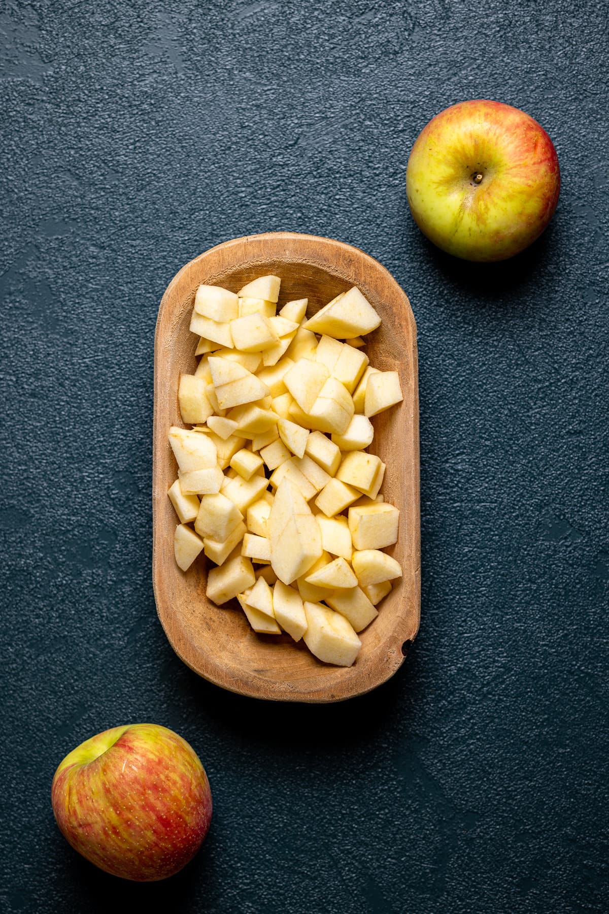 Wooden bowl of apple pieces next to apples