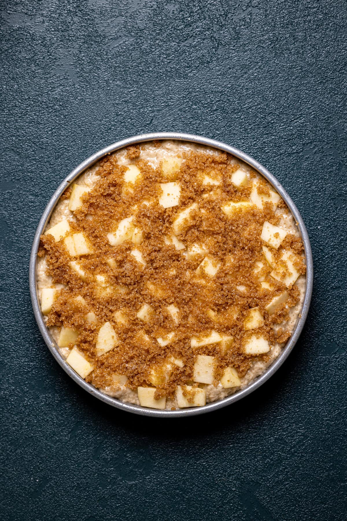 Circle pan of Apple Cinnamon Olive Oil Cake batter topped with apple pieces and topping