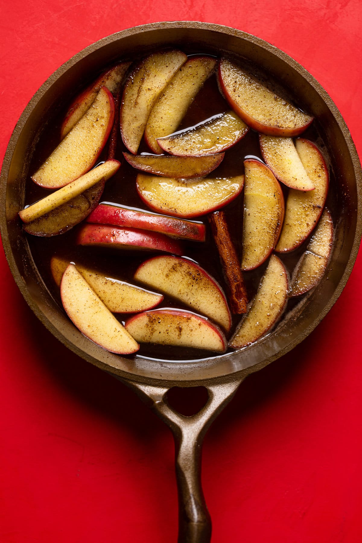 Seasoned apple slices floating in a pan with cinnamon sticks