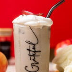 Apple Crisp Oatmilk Latte with a straw in a glass that has "Grateful" written on it