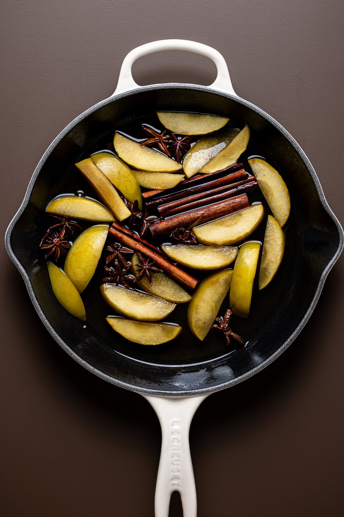 Apple slices and spices floating in a pan of water