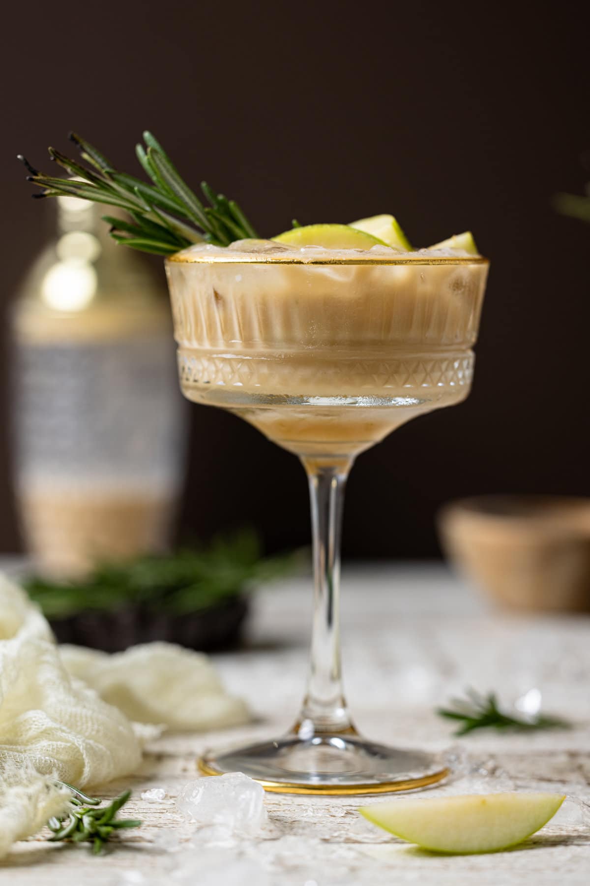 Apple Caramel Espresso Martini in a long-stemmed glass topped with a sprig of rosemary and apple slices