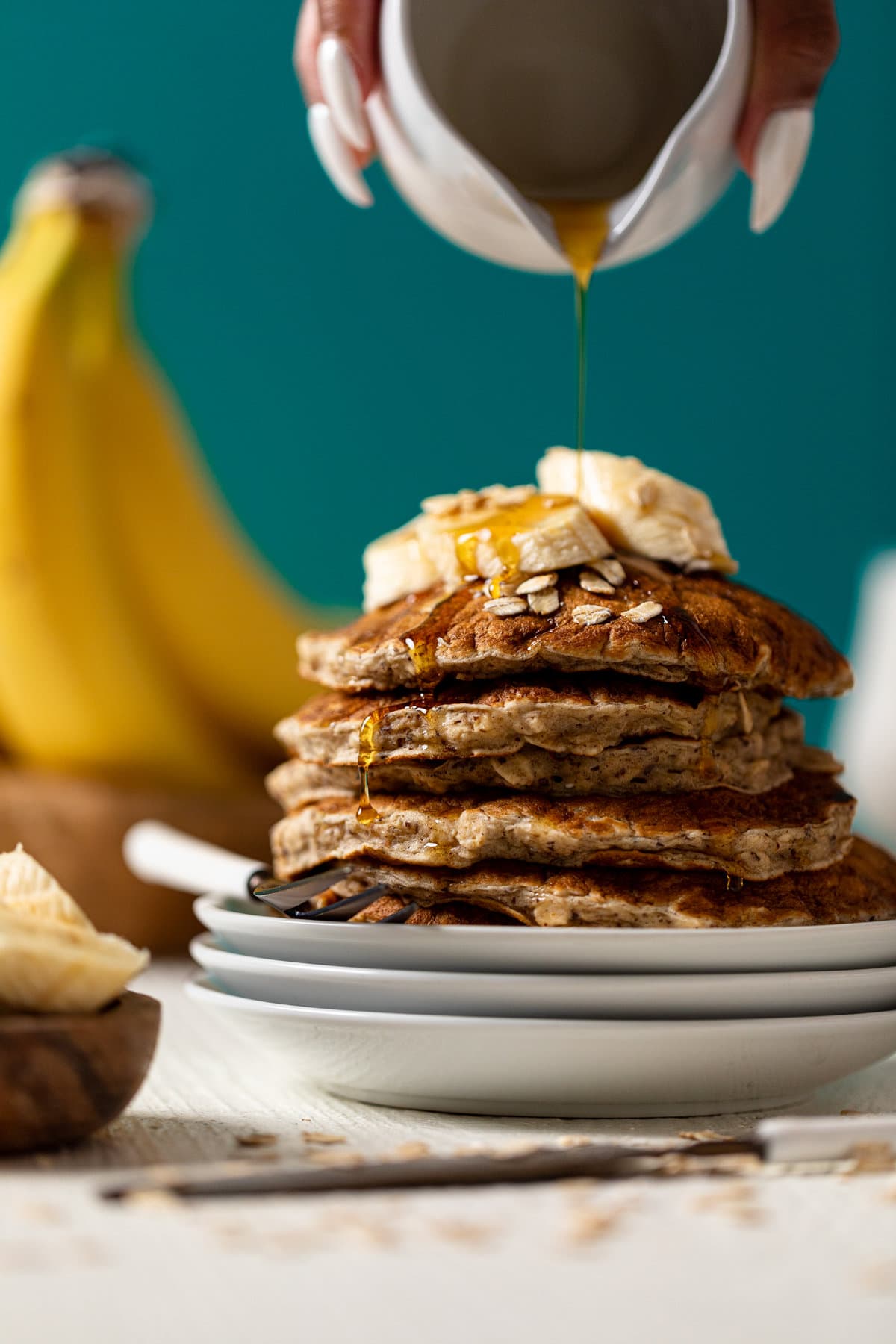 Syrup pouring onto a stack of Fluffy Banana Oat Pancakes