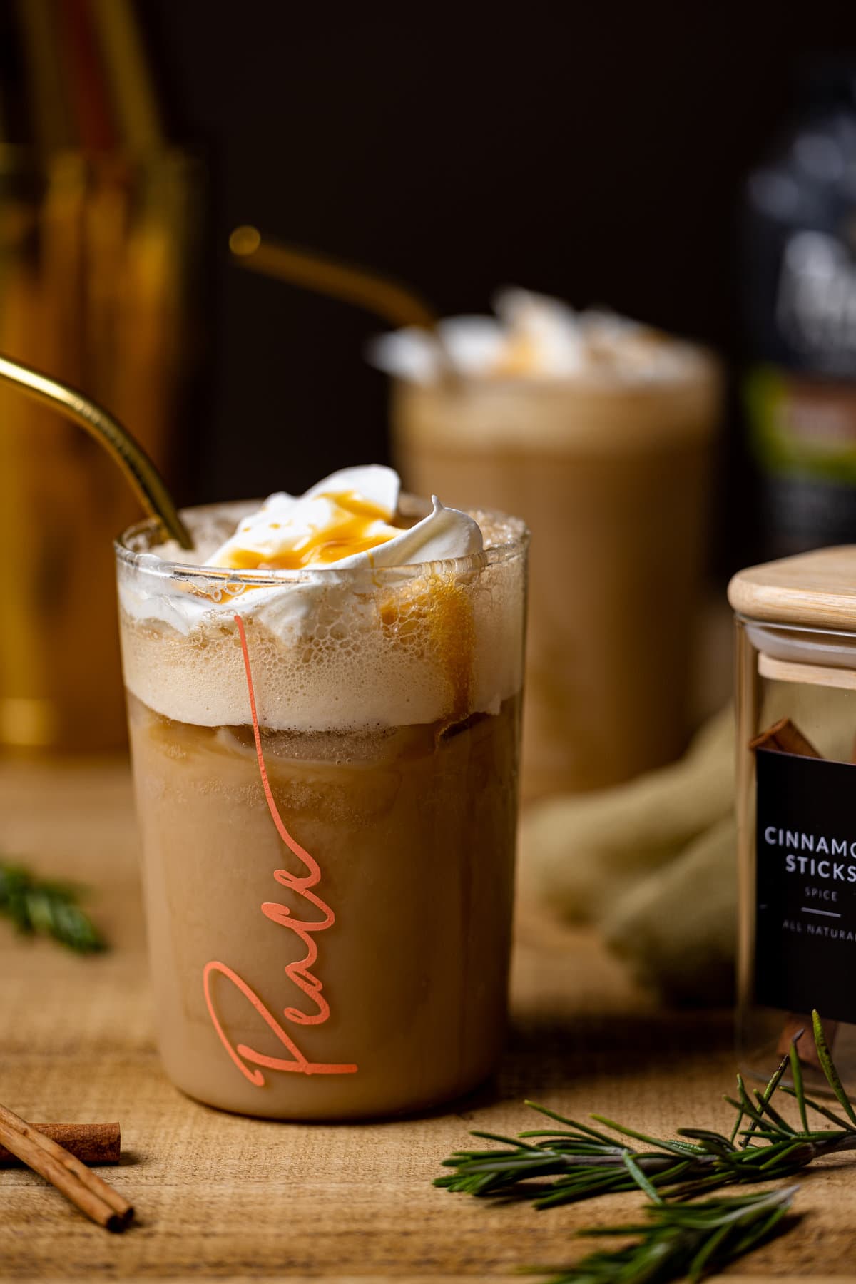 Iced Brown Sugar Shaken Espresso in a glass with \"Peace\" written on it next to a jar of cinnamon sticks