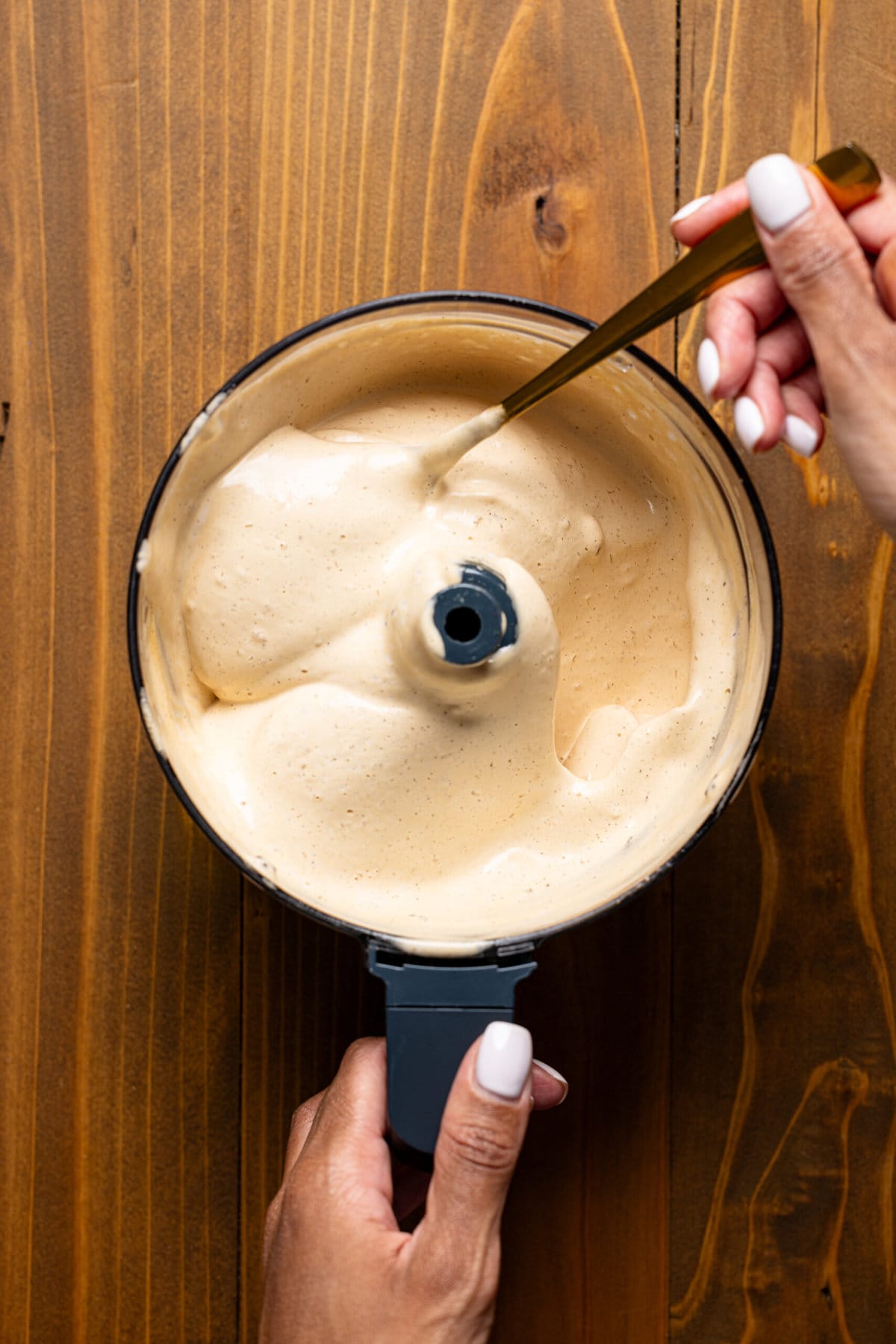 Whipped latte in a food processor with a spoon being held.
