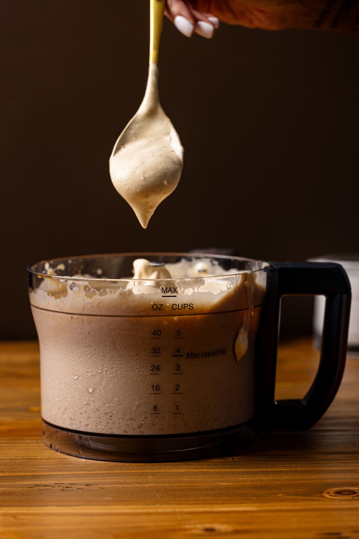 Front view of whipped coffee in a food processor being held up with a spoon.