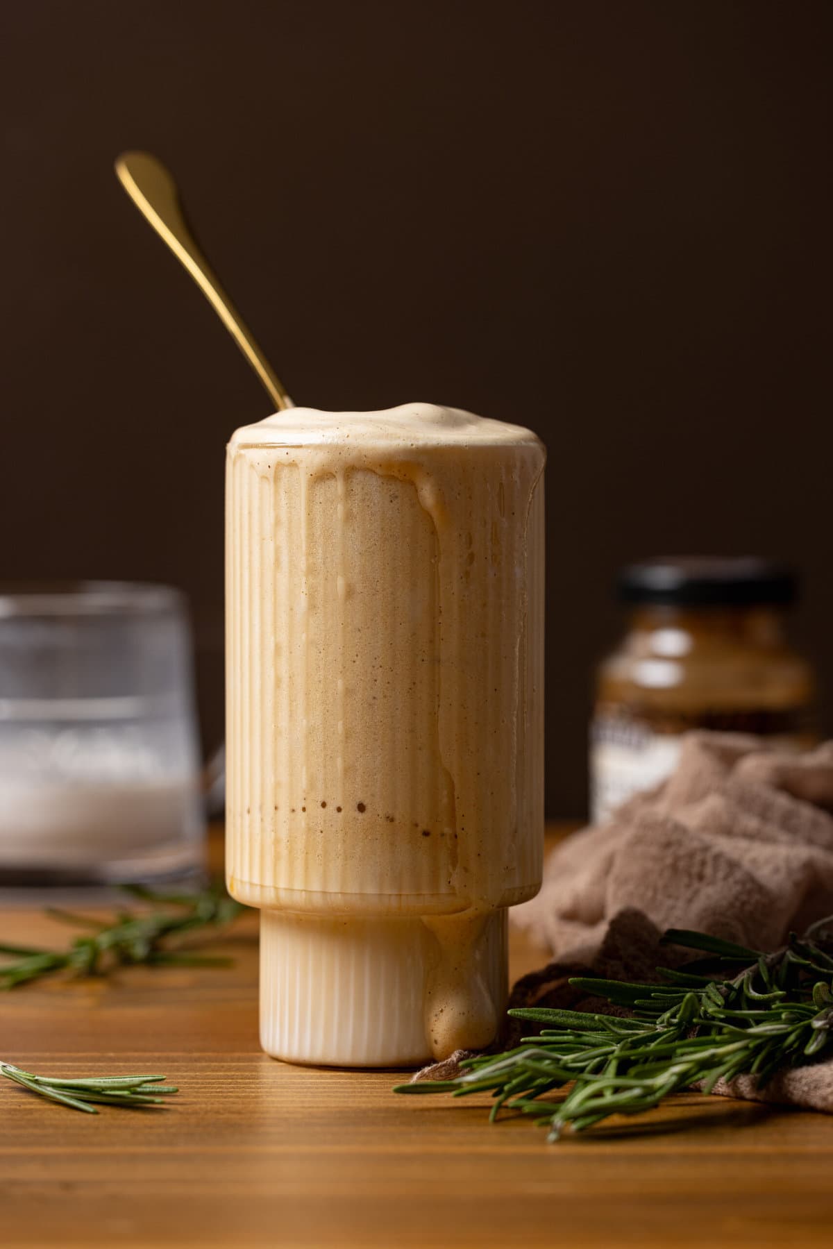 Dalgona iced vanilla coffee in a glass with a spoon and milk in the background. 